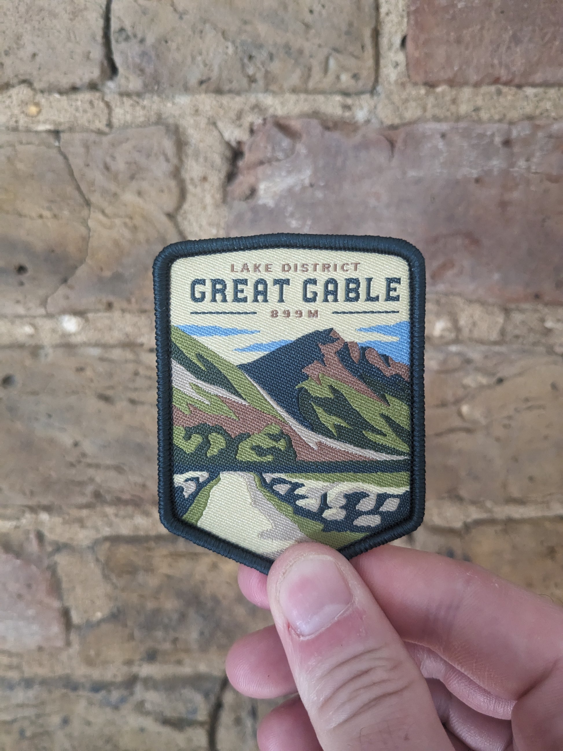 Image of the Great Gable badge being held up against a brick wall backdrop.