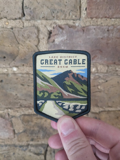 Image of the Great Gable badge being held up against a brick wall backdrop.