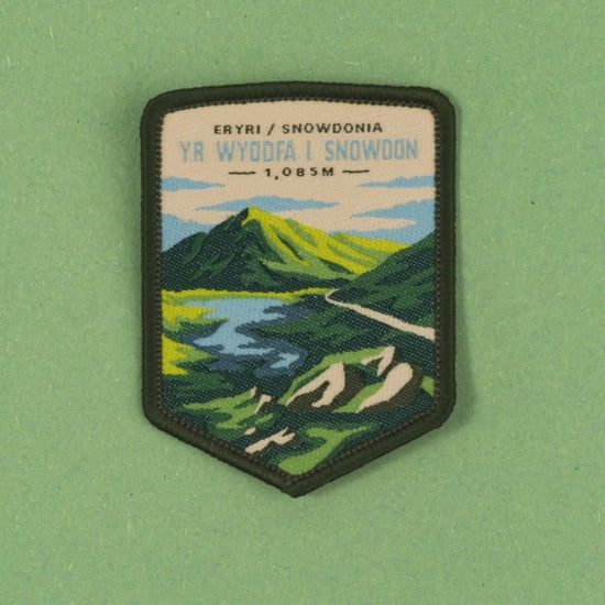 video depicting the Snowdon patch on a backing card, jumping onto a bag and being applied via the easy iron on backing